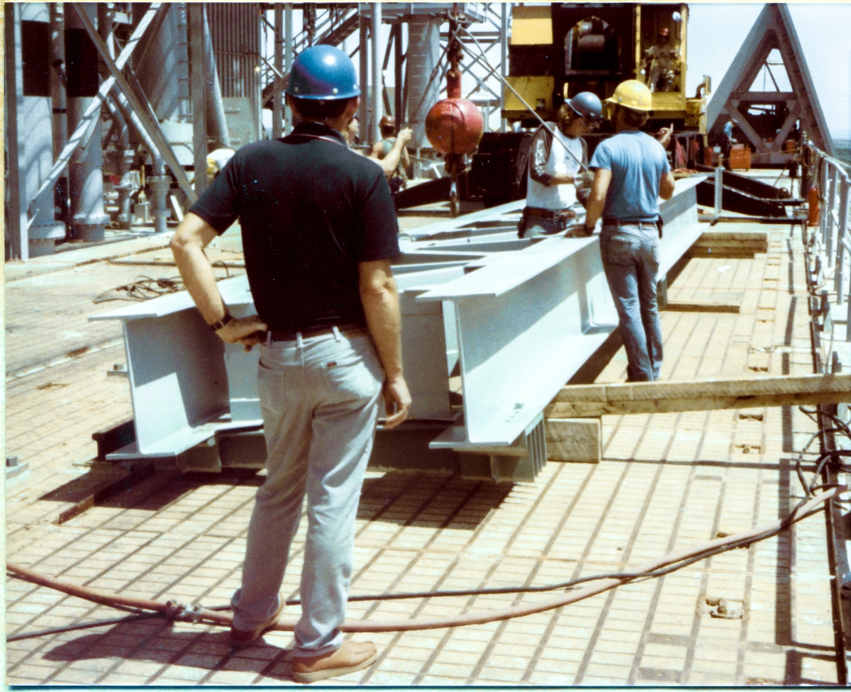 Image 070. Wade Ivey (back to camera) watches closely as his general foreman Rink Chiles (yellow hardhat), along with Rink's brother Reuben Chiles (bue hardhat) attach a lifting sling to the strongback which will be hung on existing iron at the top of the Fixed Service Structure at Space Shuttle Launch Complex 39-B, Kennedy Space Center, Florida, for the purposes of stiffening up the FSS, to permit subsequent attachment of the Gox Arm, via a pair of large hinges that will be bolted on to it after it is installed. Wade was extraordinarily savvy in the ways of ironworking, and was an ex-ironworker himself, and after he created his own steel erection company, Ivey Steel, he, along with a host of Union Ironworkers from Local 808, did what was generally agreed upon by NASA contracting management personnel, to be the best steel erection work out on the Cape, which was one of the most difficult steel erection environments that could be found anywhere, due to the exceedingly close-tolerance and high-complexity nature of the space programs work which was done out there. Photo by James MacLaren.